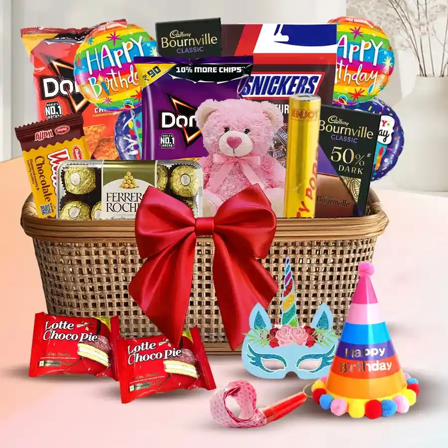 Exclusive gift basket featuring chocolates, a teddy bear, savory snacks, party accessories, and vibrant balloons, all beautifully arranged with a red bow.