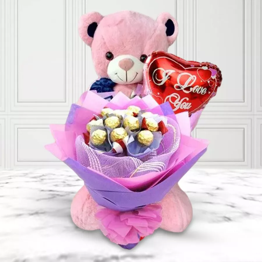 A plush teddy bear next to a bouquet of Ferrero Rocher chocolates and a "I Love You" Mylar balloon.