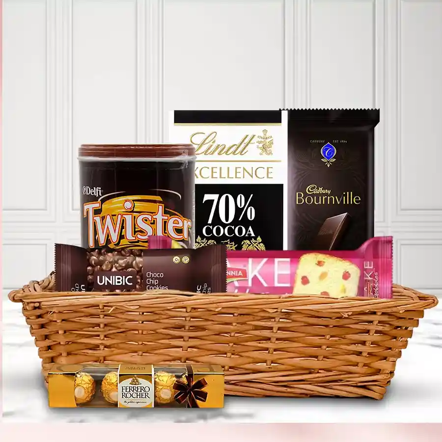 Scrumptious chocolates gift basket for Mother's Day containing Britannia Fruits Cake, Cadbury Bournville, Lindt bars, Twister wafers, Unibic Choco Chip Cookies, and Ferrero Rocher minis, arranged in a charming cane basket.