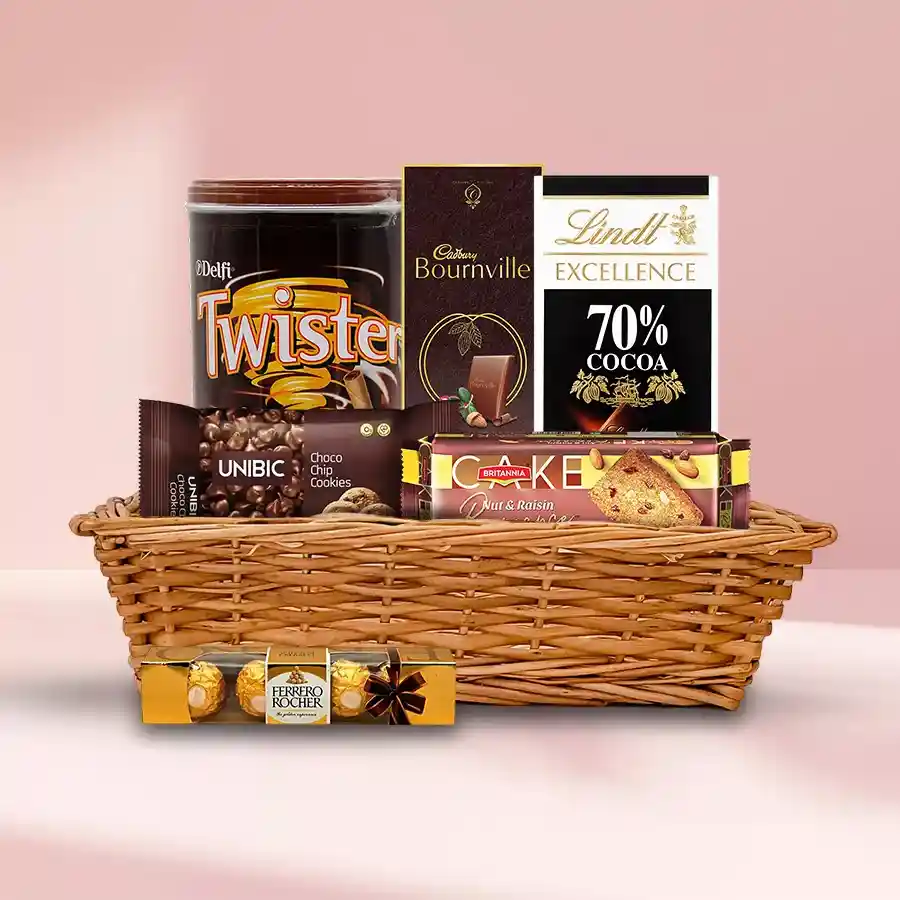 Sumptuous Chocolate Gift Hamper featuring Britannia Nuts & Raisin Cake, Lindt Excellence and Bournville bars, Twister Wafers, Unibic Choco Chip Cookies, and Ferrero Rocher chocolates arranged in a small basket.