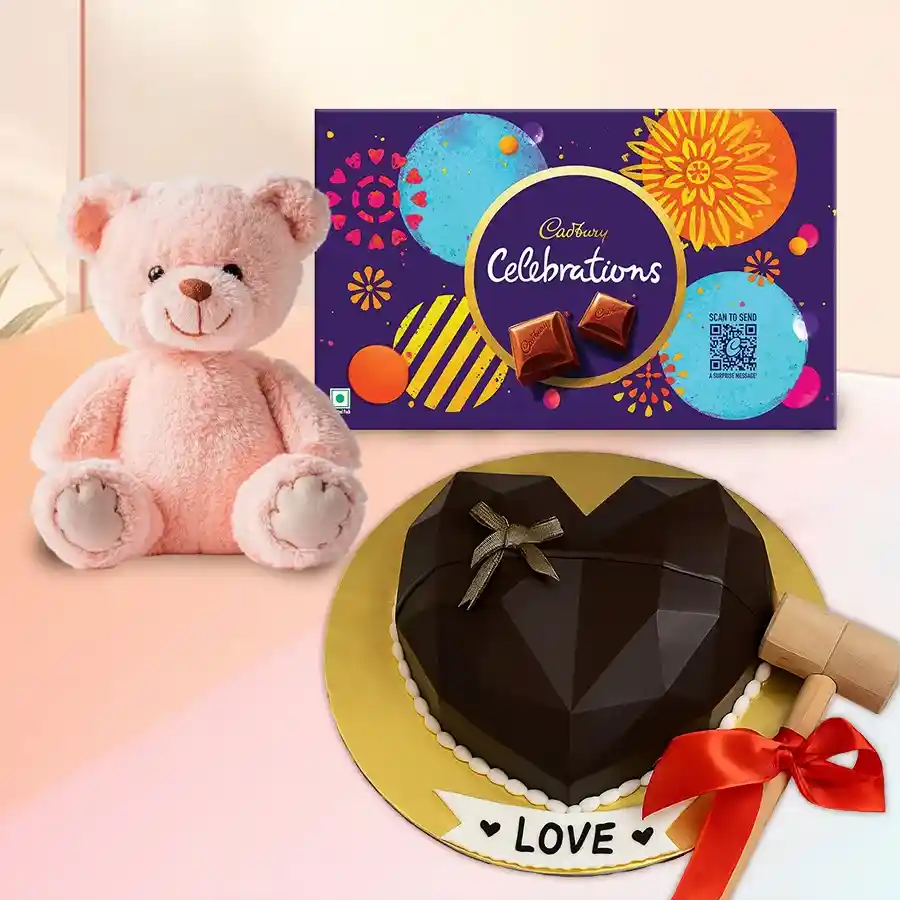 Heart-shaped piñata cake with hammer, Cadbury chocolates, and a teddy bear for celebrations.