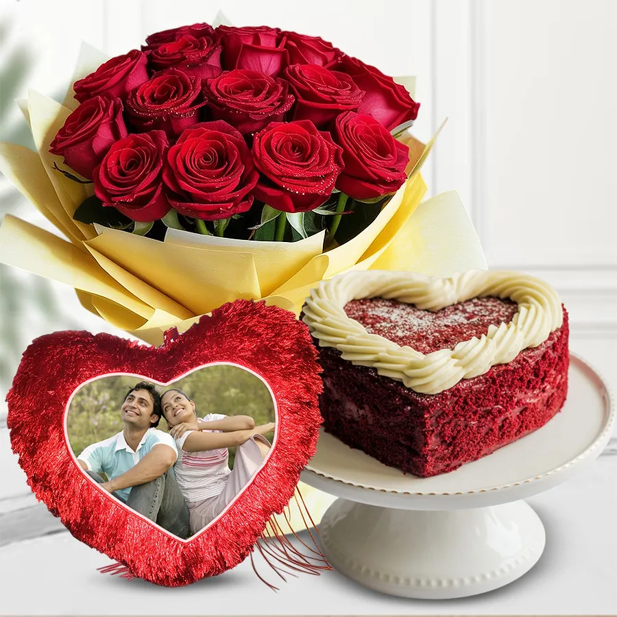 Heart-shaped red velvet cake with personalized cushion and red roses bouquet for a romantic gift.