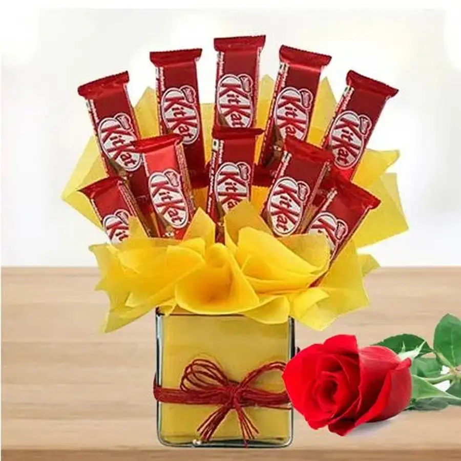 Kitkat chocolates in yellow tissue arranged in a glass vase with a single red rose.
