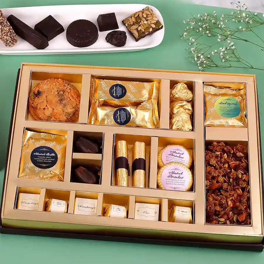 A beautifully arranged assortment of decadent treats including Florentine cookies, almond chocolate fingers, almond brittle, butterscotch-filled chocolates, granola chocolate logs, and granola, all featuring a variety of nuts and flavors.