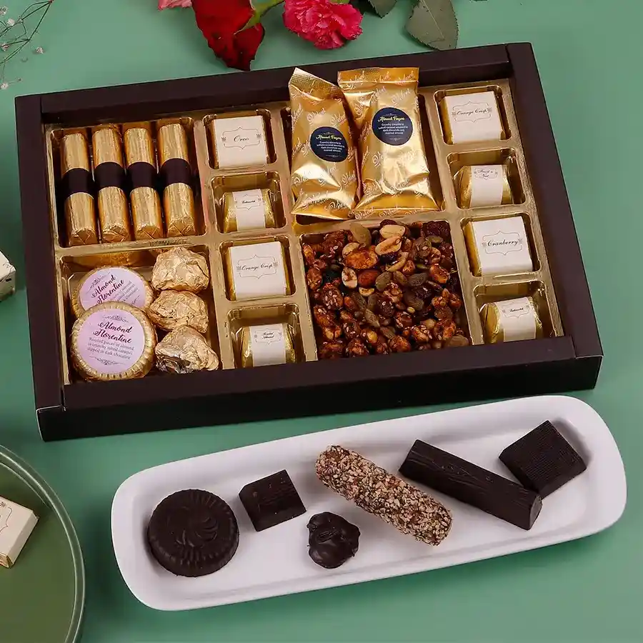 A festive box filled with a variety of chocolates and treats for Diwali, including granola chocolate logs, almond chocolate florentines, almond chocolate rocks, assorted chocolates, almond fingers, and a spicy sweet trail mix.
