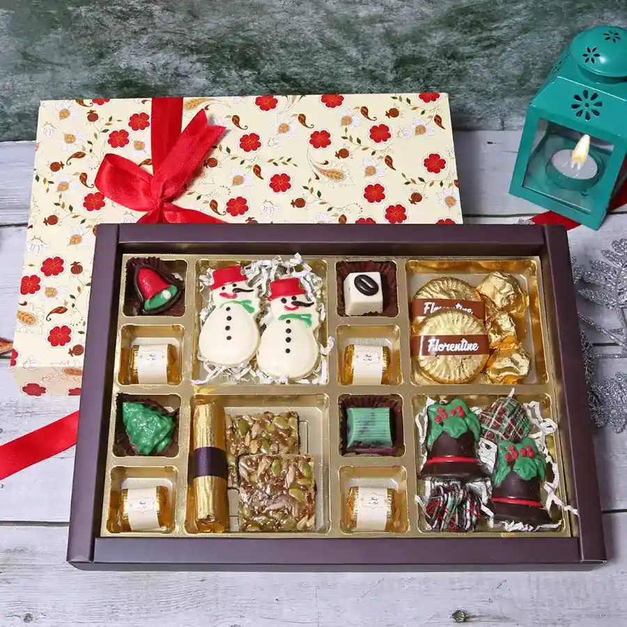 Christmas Chocolate Celebration Box featuring a festive mix of assorted chocolates, florentines, chocolate rocks, strawberry chocolate log, mini snowmen, and chocolate bells arranged in a decorative box.