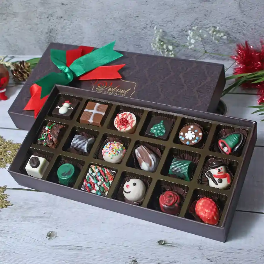 A beautifully arranged box of Christmas Special Chocolaty Confections featuring an assortment of soft-filled chocolates, brownie bites, nutty treats, and chocolate truffles, set against a festive backdrop.
