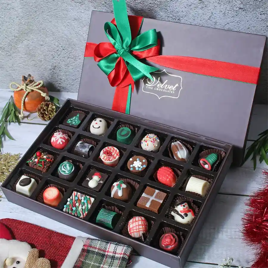 A beautifully presented box of assorted Christmas chocolates featuring an elegant design, with an array of soft-filled chocolates, brownie bites, nutty chocolates, and truffles displayed elegantly.