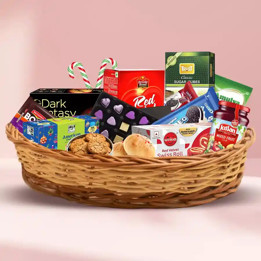 A beautifully arranged cane basket filled with an assortment of exotic Christmas treats, including rich fruit cake, chocolates, Swiss rolls, assorted biscuits, cookies, jams, caramels, and tea.