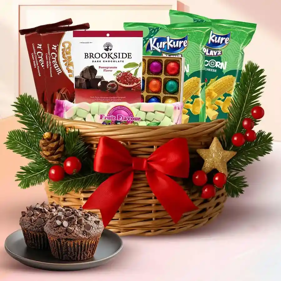 Delightful Christmas Celebration Gift Basket filled with sweet and savory treats, including Chocochip Muffins, Tiffany Choco Wafers, Brookside Pomegranate Chocolate, Kurkure Puffcorn, marshmallows, and handmade chocolates, presented in a festive cane basket with Christmas accents.
