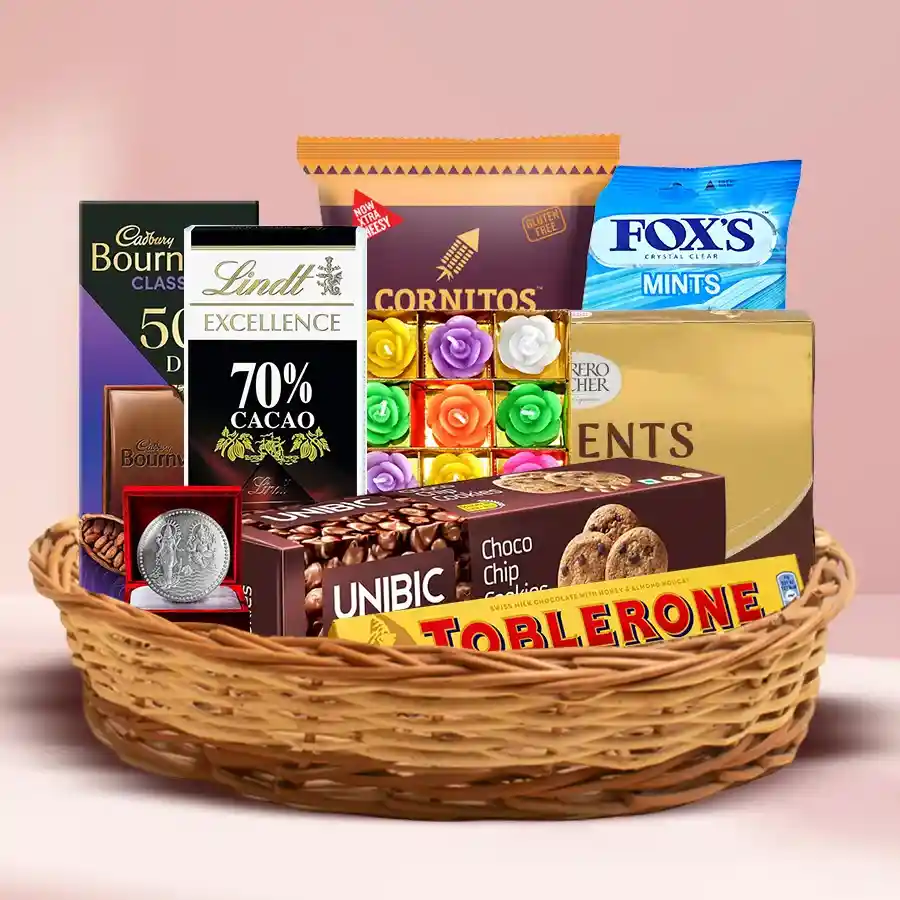 Exclusive Diwali Chocolates and Snacks Hamper featuring Ferrero Rocher, Lindt Excellence chocolates, Unibic Choco Chip Cookies, Cornitos Nachos, Foxes Mint Candy, decorative wax candles, and a silver-plated Ganesh-Laxmi coin in a reusable cane basket.