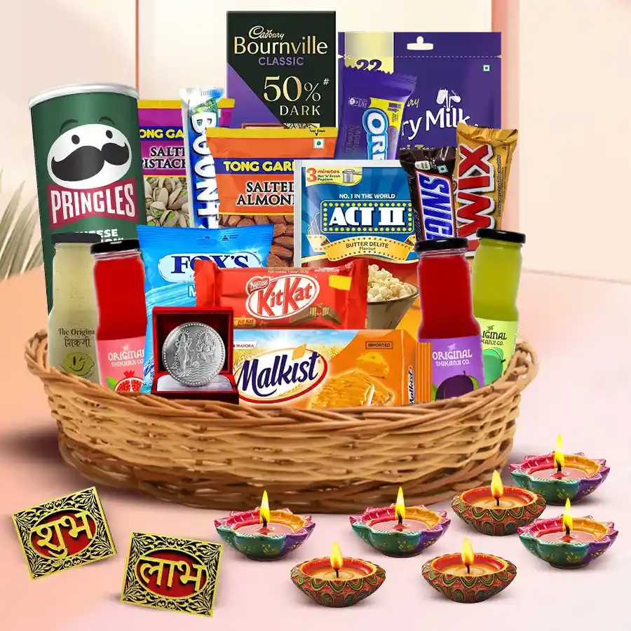 A beautifully arranged Diwali hamper containing roasted nuts, chocolates, savory snacks, designer diyas, wall stickers, and a silver-plated Ganesh Laxmi coin, all in a reusable cane basket.