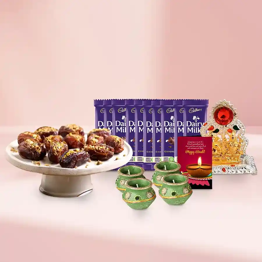 A decorative basket filled with Supreme Dates Baklava, Cadbury Dairy Milk bars, decorated wax diyas, and a Ganesh Laxmi Mandap, topped with a Diwali card.