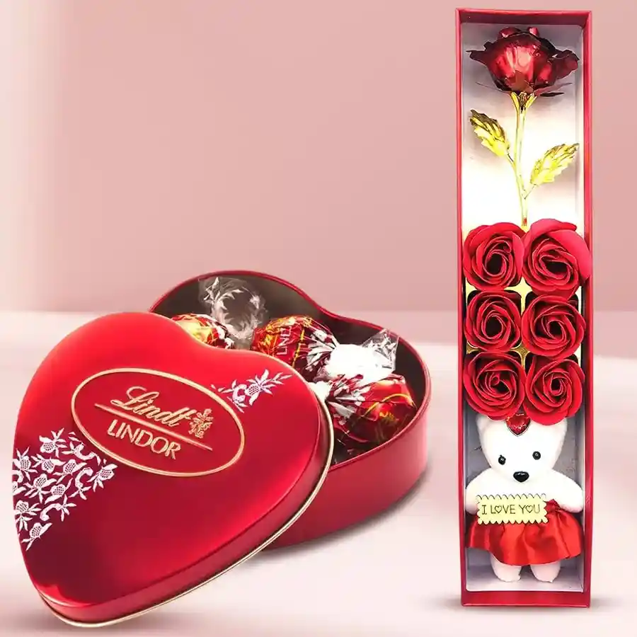 Valentine's Day surprise box featuring a red artificial rose, a teddy bear, a luxurious scented perfume, and a Lindt Lindor chocolate box.