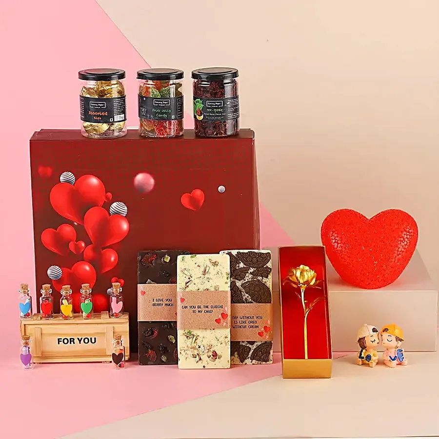 Scrumptious hamper filled with chocolates, a golden rose, LED heart light, kissing couple statue, message bottle, paan gulkand, fruit jelly, and a greetings card, arranged in an elegant gift box.