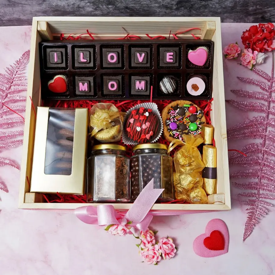 A beautifully arranged Mother's Day hamper filled with assorted chocolates and cookies, including a 12-piece chocolate box, chocochip cookies, florentines, coated raisins, butterscotch, chocolate logs, almond rocks, pizzokie cookie, and a hot chocolate bomb.